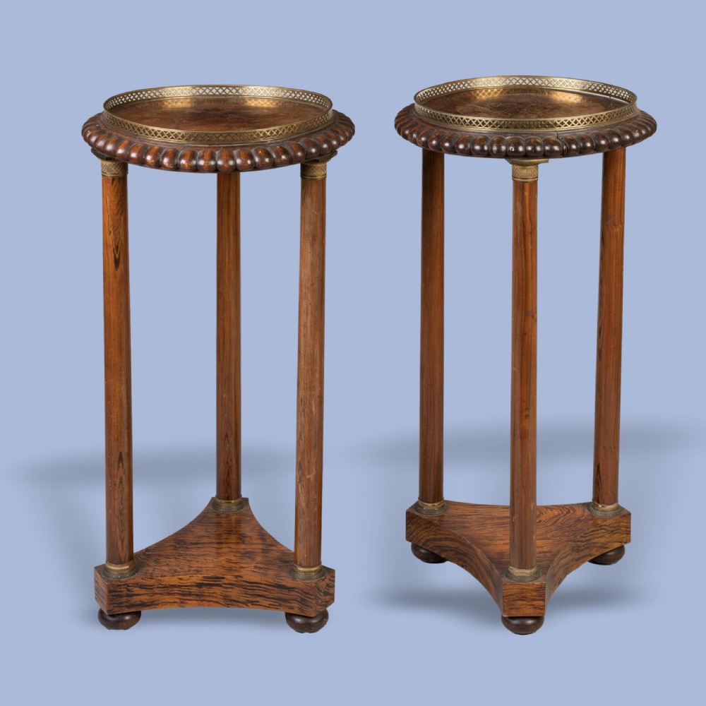 A pair of tall French Empire style mahogany pedestals featuring brass gallery rims, gadrooned tops, three cylindrical columns, and tri-form bases resting on bun feet.