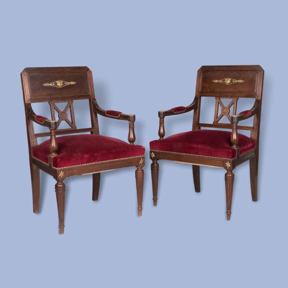 A pair of French Consulate style mahogany armchairs with red velvet upholstery, fluted front legs, and decorative brass star mounts.