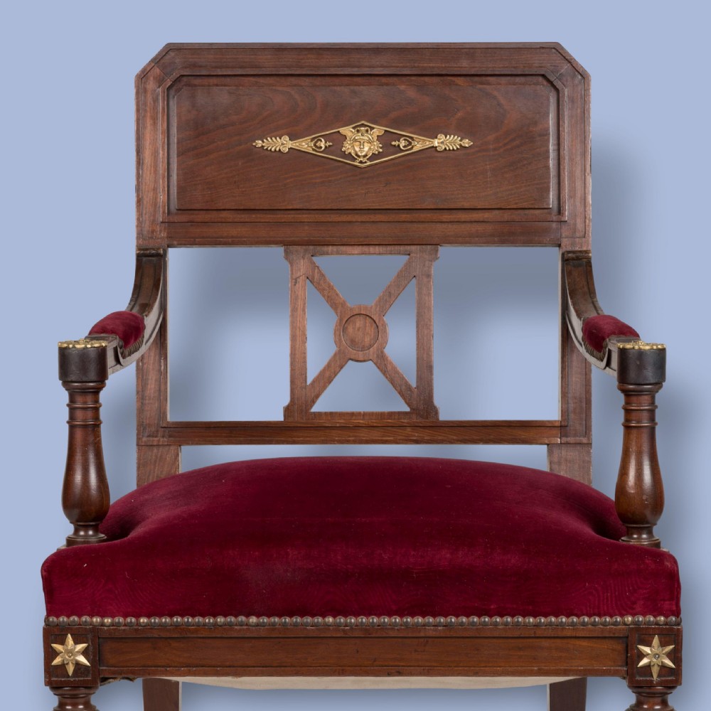 A pair of French Consulate style mahogany armchairs with red velvet upholstery, fluted front legs, and decorative brass star mounts. View II