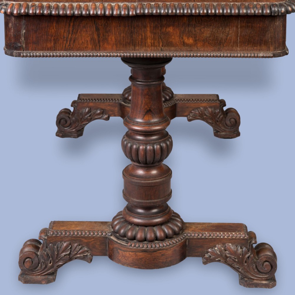 A Late Georgian rosewood writing table featuring a rectangular top with carved egg-and-dart moulding, resting on twin turned column pedestals and carved scroll feet. View IV