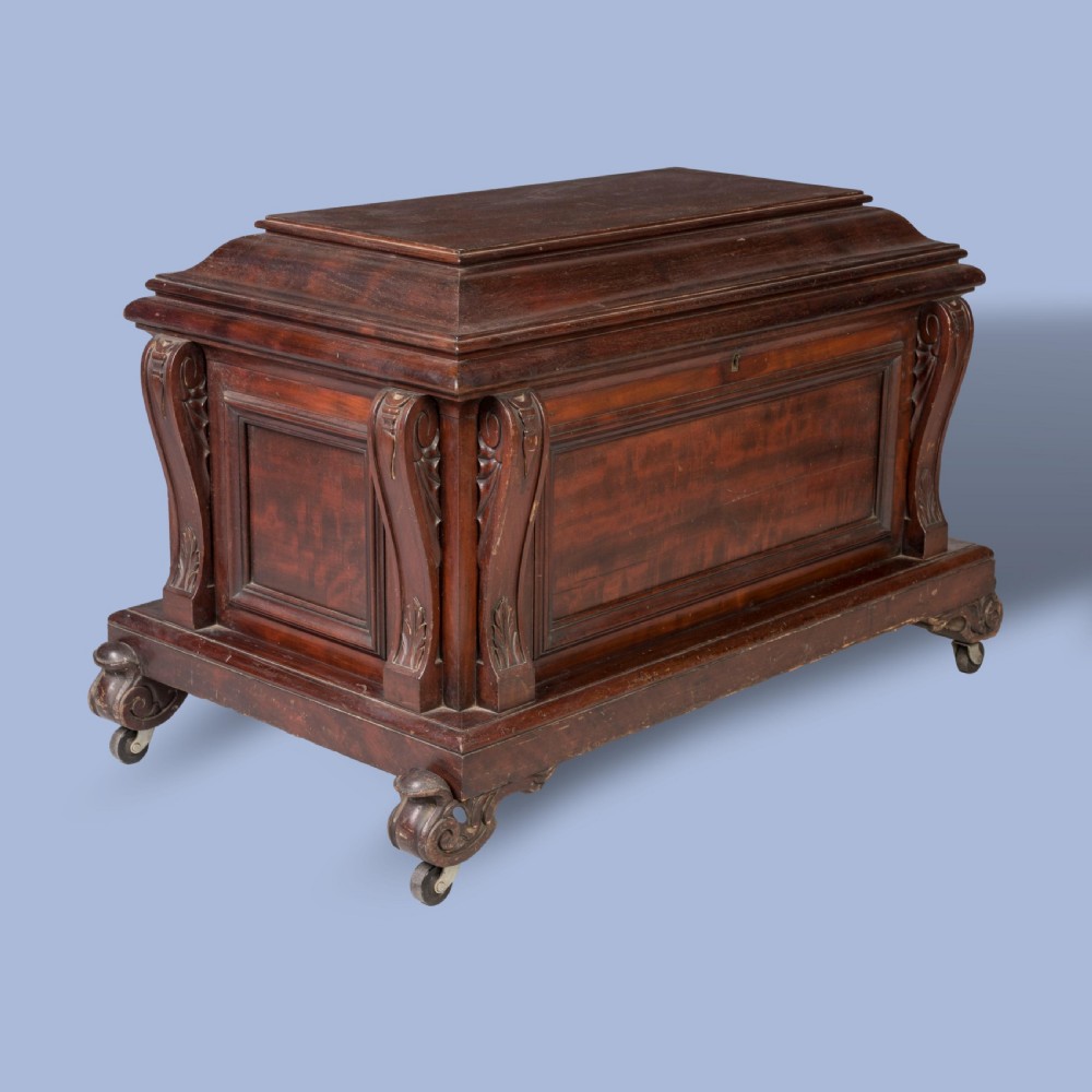 A William IV mahogany sarcophagus cellarette with carved scroll corner pilasters, panelled sides, and castors.
