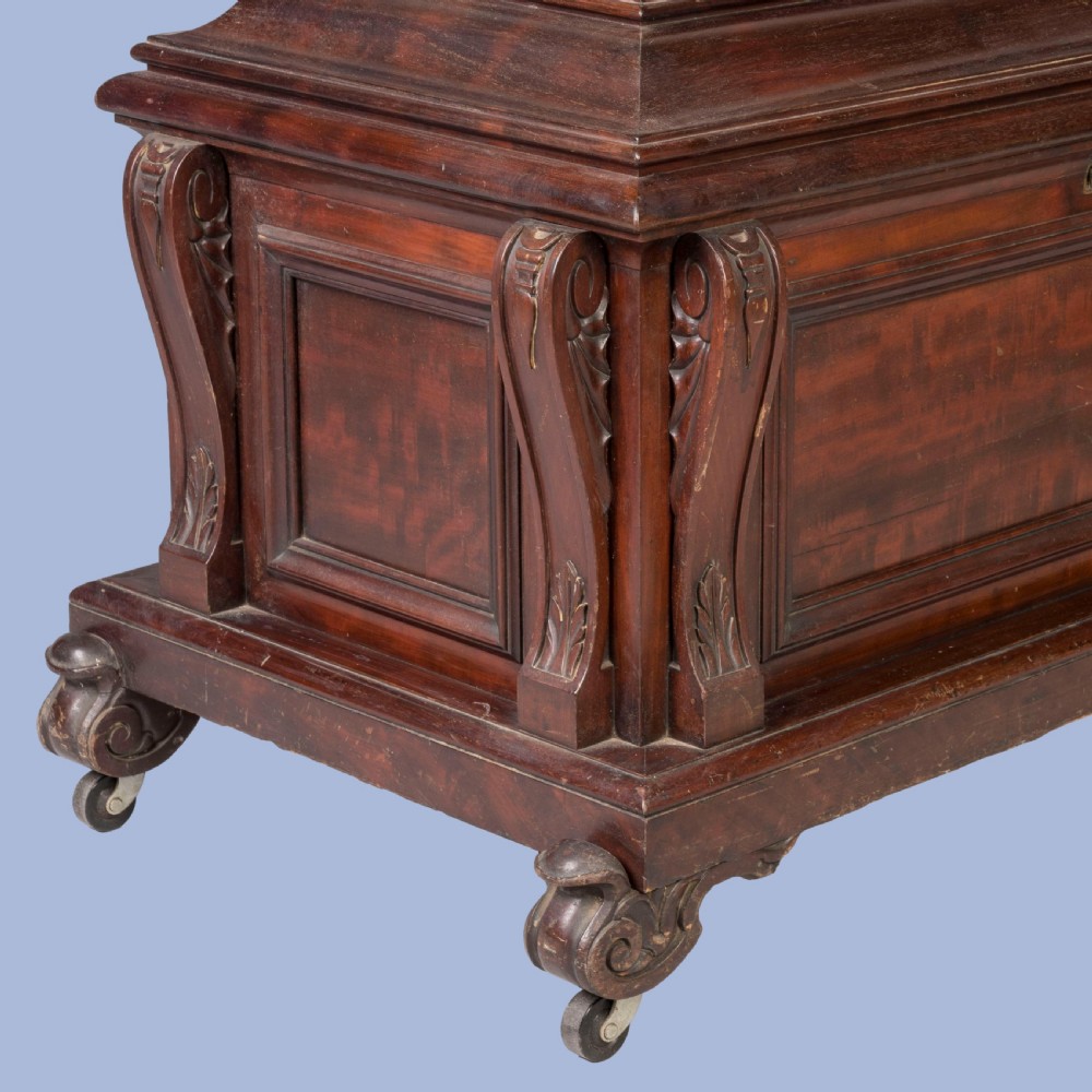 A William IV mahogany sarcophagus cellarette with carved scroll corner pilasters, panelled sides, and castors. View V
