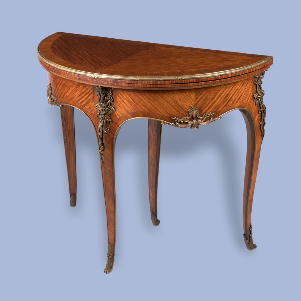 A French Louis XV style demilune kingwood card table featuring curved cabriole legs, intricate parquetry veneer, and decorative gilt-bronze mounts.