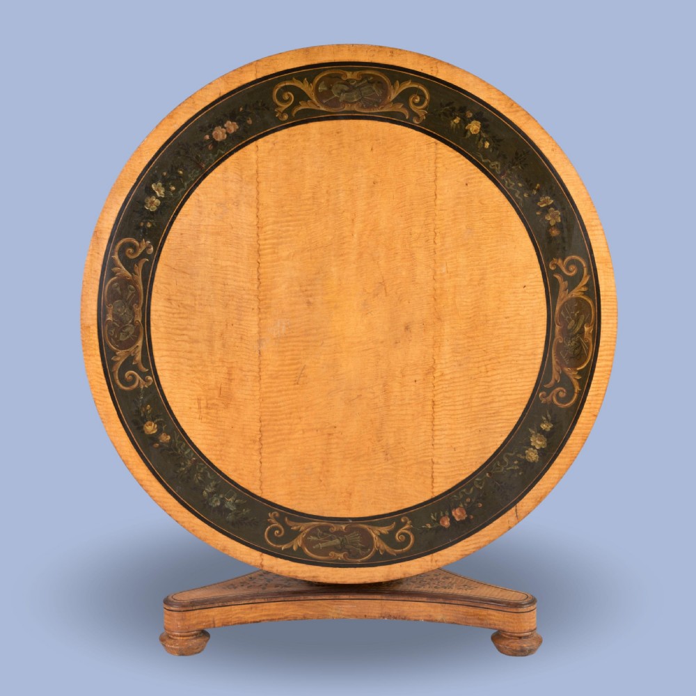 A Regency period circular centre table crafted from light sycamore with hand-painted floral borders resting on a central pedestal and triform base. View II
