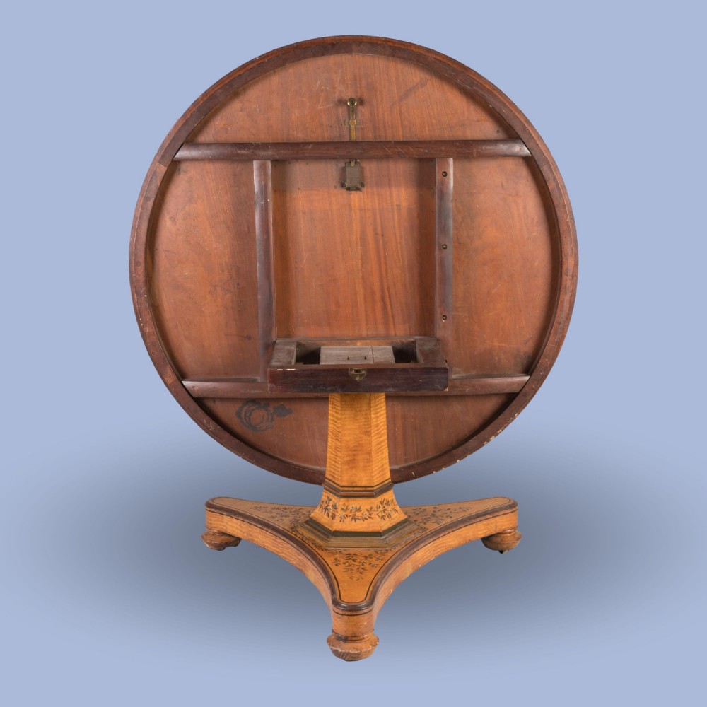 A Regency period circular centre table crafted from light sycamore with hand-painted floral borders resting on a central pedestal and triform base. View III