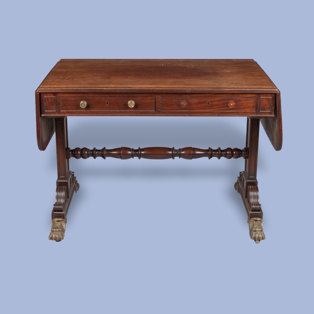 A Regency period dark mahogany sofa table featuring two frieze drawers, drop leaves, a turned stretcher, and splayed legs with brass paw feet.