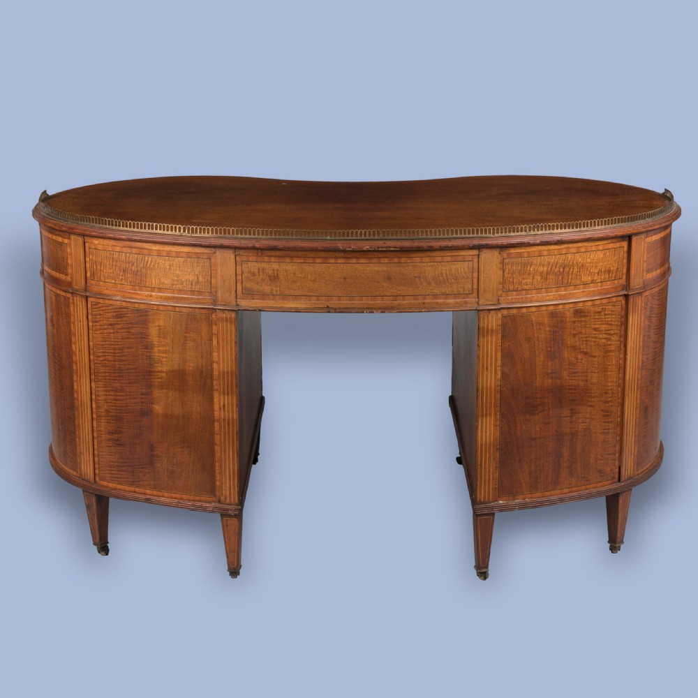 A late 19th-century mahogany kidney-shaped desk featuring satinwood inlay, brass drawer handles, a perforated brass top gallery, and tapered legs with brass castors. View III