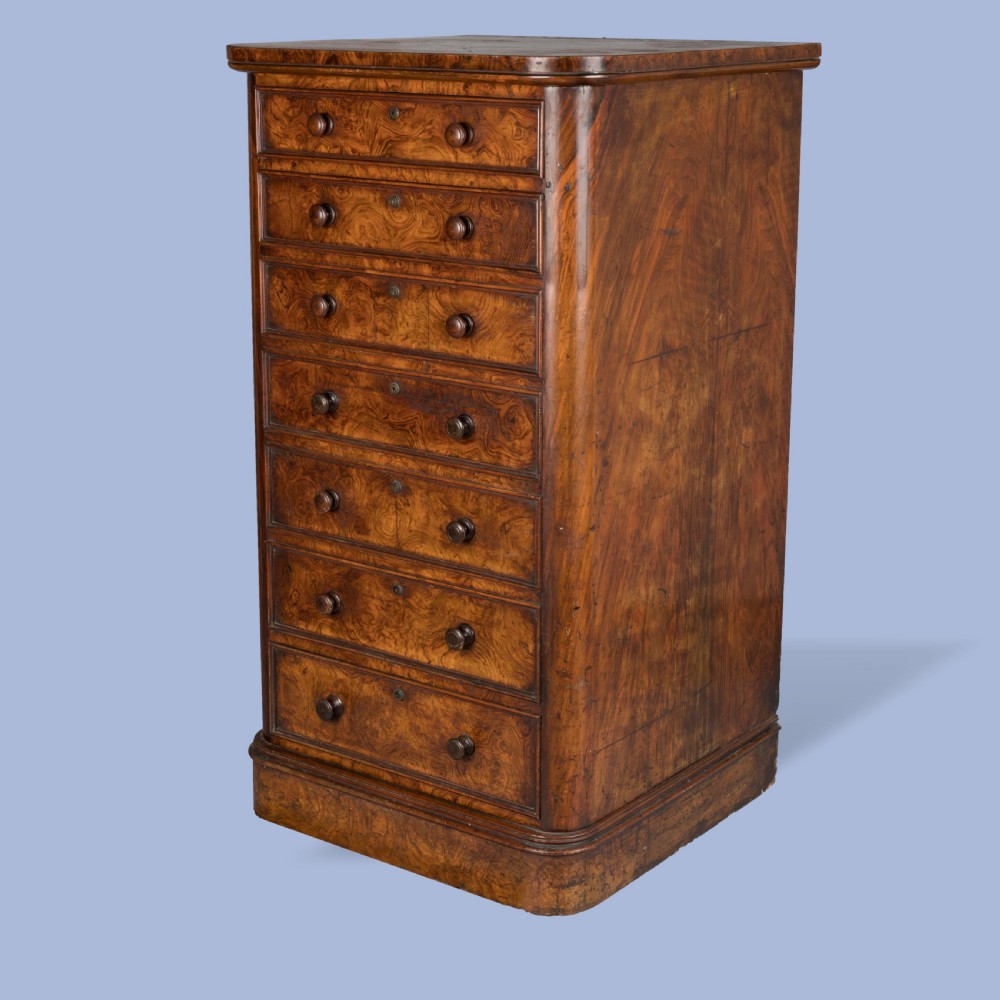 A tall Victorian burr walnut Wellington chest featuring seven graduated drawers, turned knobs, a locking side bar, and a plinth base.