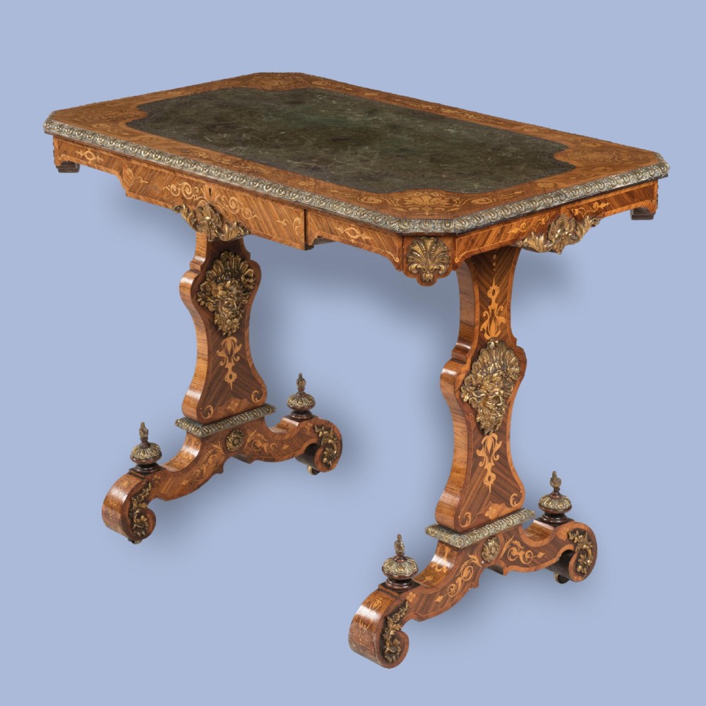 An ornate 19th-century French style marquetry writing table featuring a green leather top, gilt-bronze mounts, and scrolled end supports.