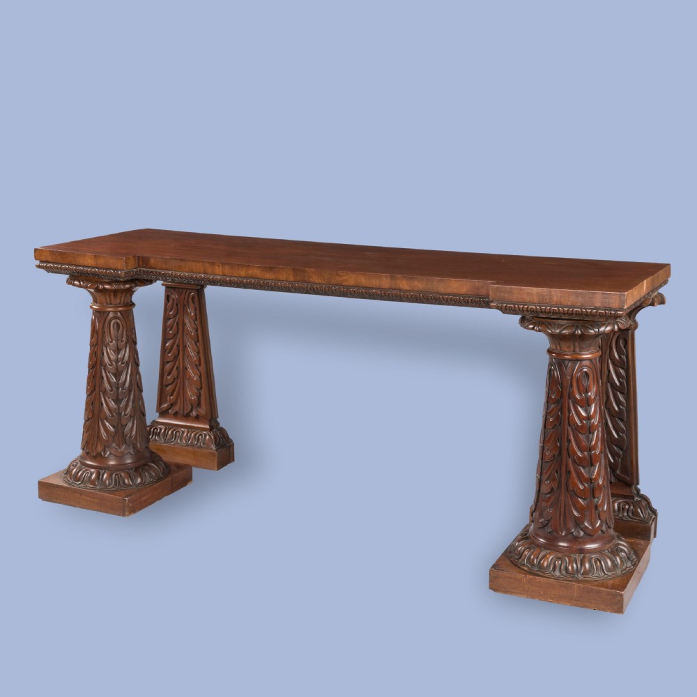 A William IV mahogany serving table featuring a rectangular top, gadrooned edge trimming, and acanthus leaf carved column supports on plinth bases.