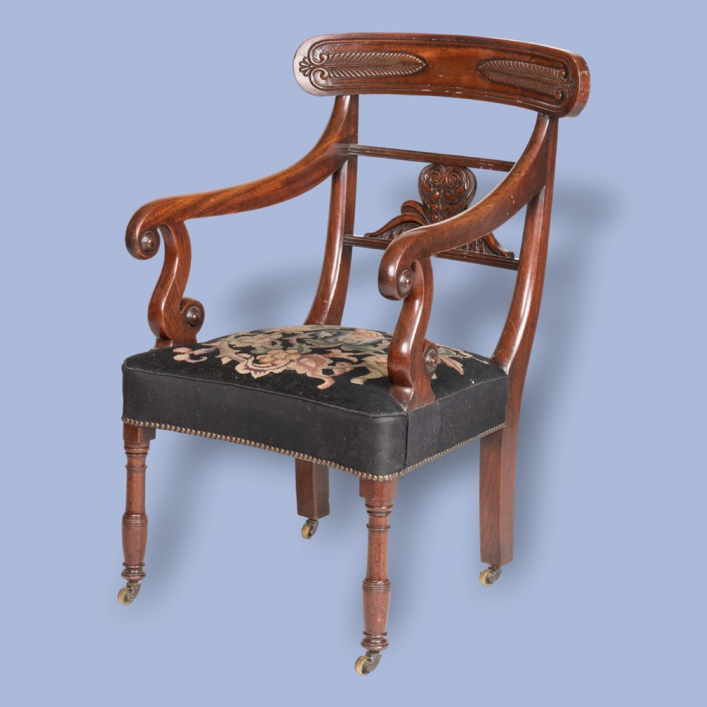 A William IV mahogany armchair featuring a carved top rail, curved scroll armrests, turned front legs on brass castors, and floral tapestry seat upholstery.