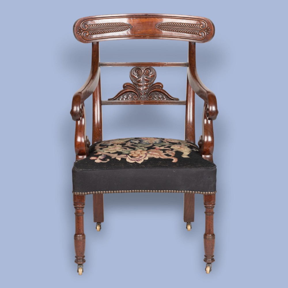 A William IV mahogany armchair featuring a carved top rail, curved scroll armrests, turned front legs on brass castors, and floral tapestry seat upholstery. View II