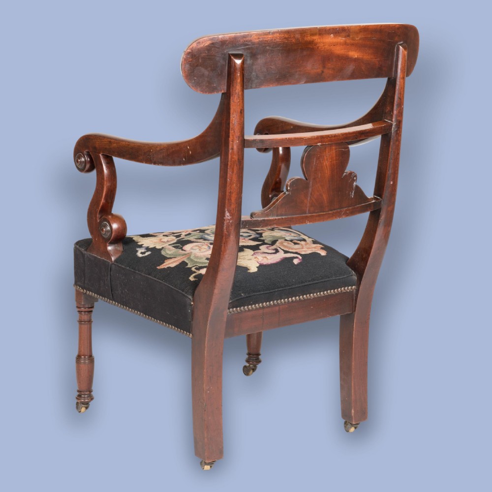 A William IV mahogany armchair featuring a carved top rail, curved scroll armrests, turned front legs on brass castors, and floral tapestry seat upholstery. View V