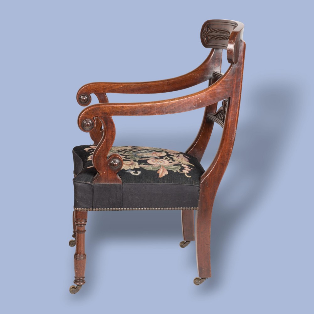 A William IV mahogany armchair featuring a carved top rail, curved scroll armrests, turned front legs on brass castors, and floral tapestry seat upholstery. View VI