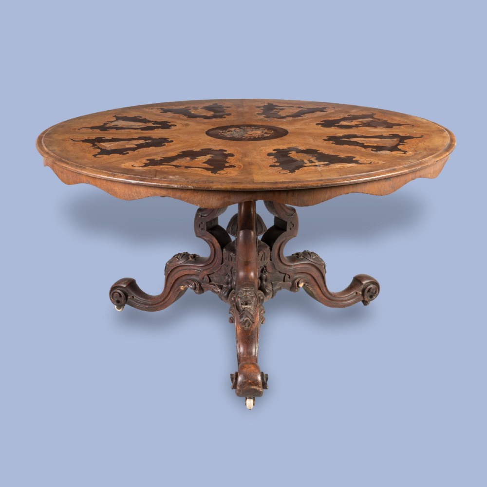 A circular Victorian walnut centre table featuring radial marquetry inlays on top and an intricately carved quadruped pedestal base with scroll feet on castors.