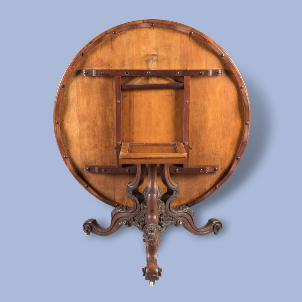 A circular Victorian walnut centre table featuring radial marquetry inlays on top and an intricately carved quadruped pedestal base with scroll feet on castors. View II