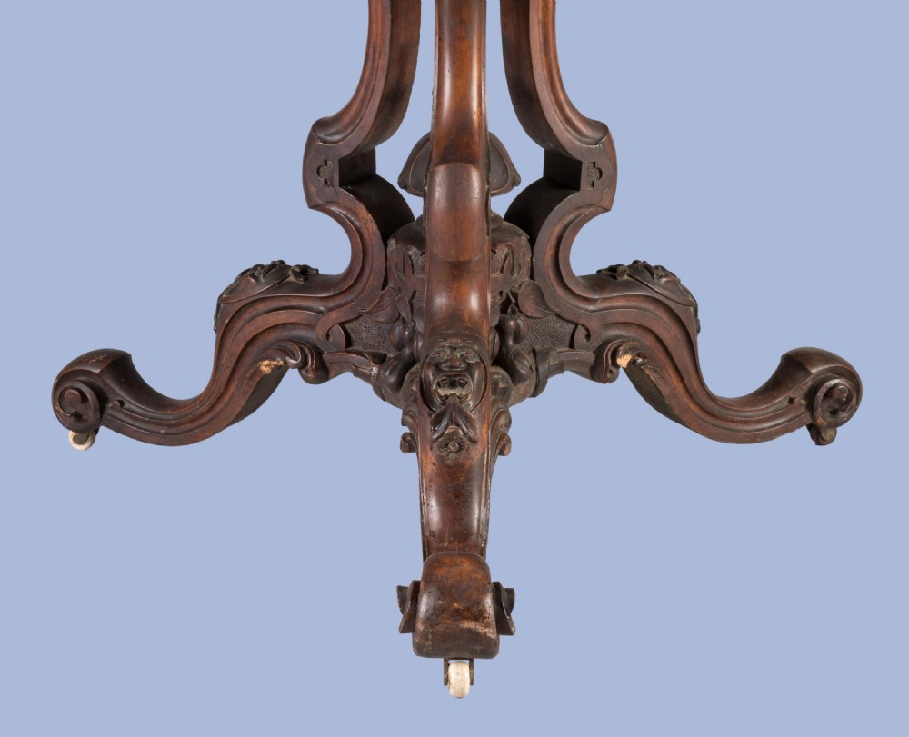 A circular Victorian walnut centre table featuring radial marquetry inlays on top and an intricately carved quadruped pedestal base with scroll feet on castors. View IV