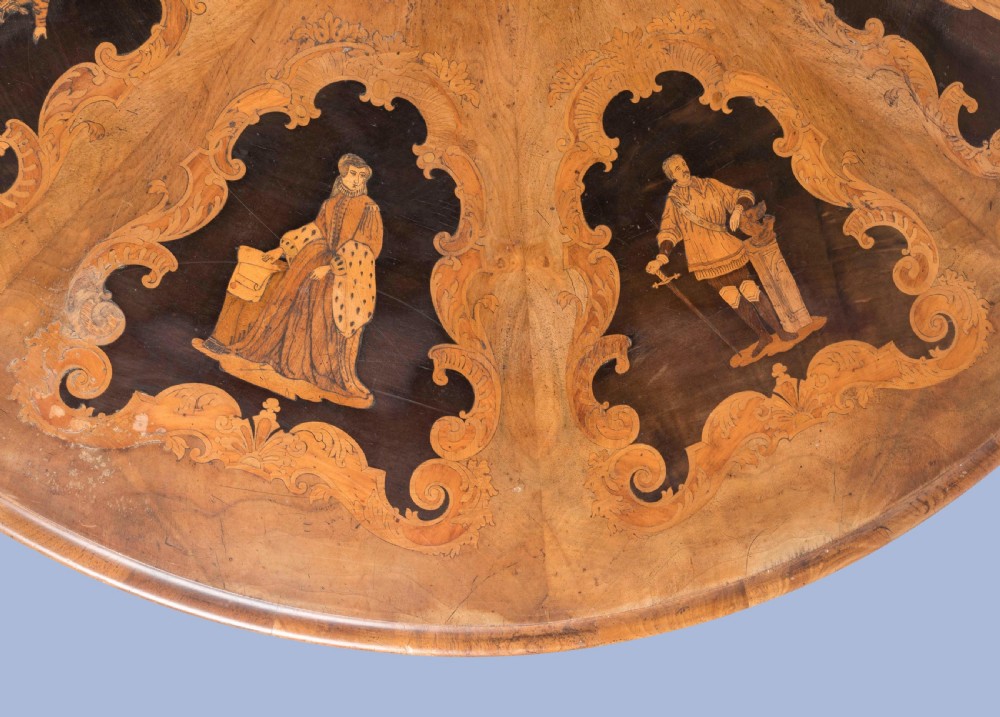 A circular Victorian walnut centre table featuring radial marquetry inlays on top and an intricately carved quadruped pedestal base with scroll feet on castors. View V