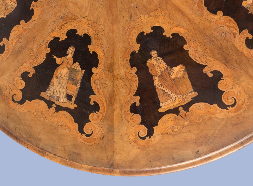 A circular Victorian walnut centre table featuring radial marquetry inlays on top and an intricately carved quadruped pedestal base with scroll feet on castors. View VI