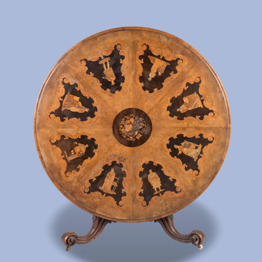 A circular Victorian walnut centre table featuring radial marquetry inlays on top and an intricately carved quadruped pedestal base with scroll feet on castors. View VII