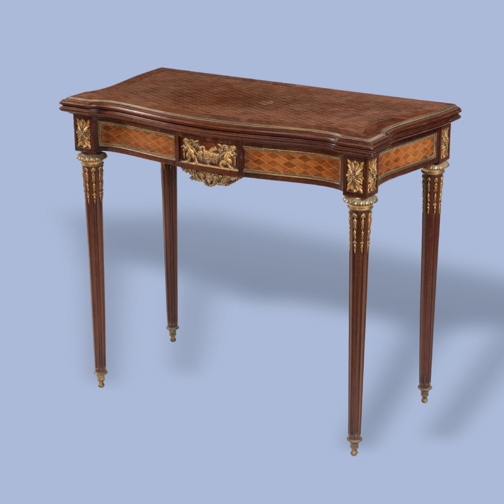 A rectangular Louis XVI style card table featuring geometric parquetry wood veneers, fluted tapering legs, and gilded ormolu mounts.