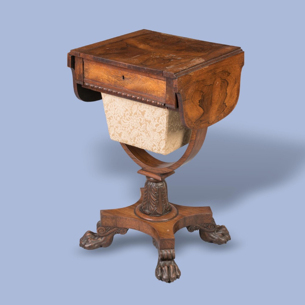 A William IV rosewood drop-leaf table with a fabric-covered work basket, U-shaped support, and carved claw feet.