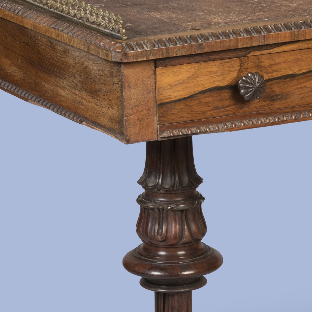 A Late Georgian rosewood writing table featuring a decorative brass gallery, an inset leather surface, two frieze drawers, and carved end supports resting on castors. View III