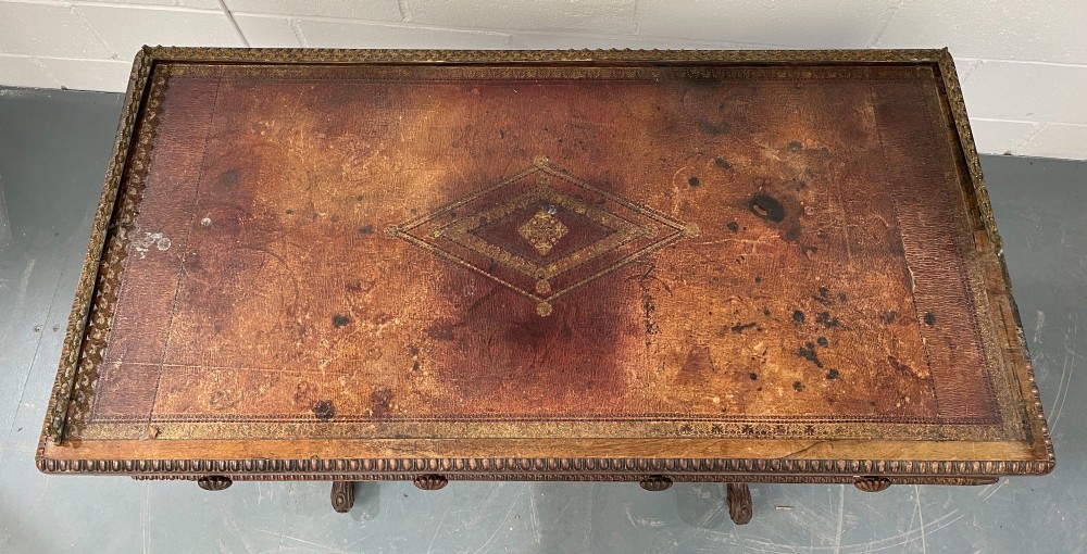 A Late Georgian rosewood writing table featuring a decorative brass gallery, an inset leather surface, two frieze drawers, and carved end supports resting on castors. View V