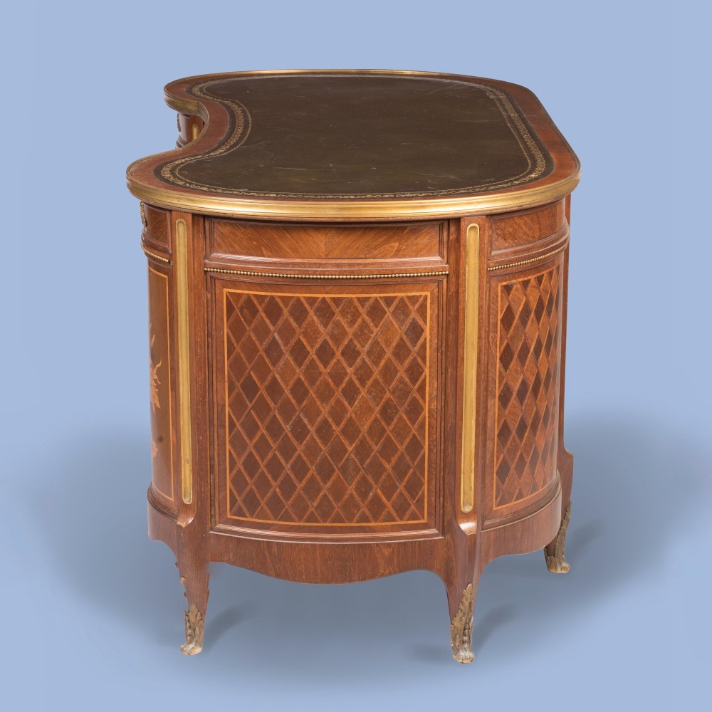 A kidney-shaped wooden writing desk featuring floral marquetry panels, gilt-bronze ormolu mounts, and a dark leather inset top with gold tooling. View V