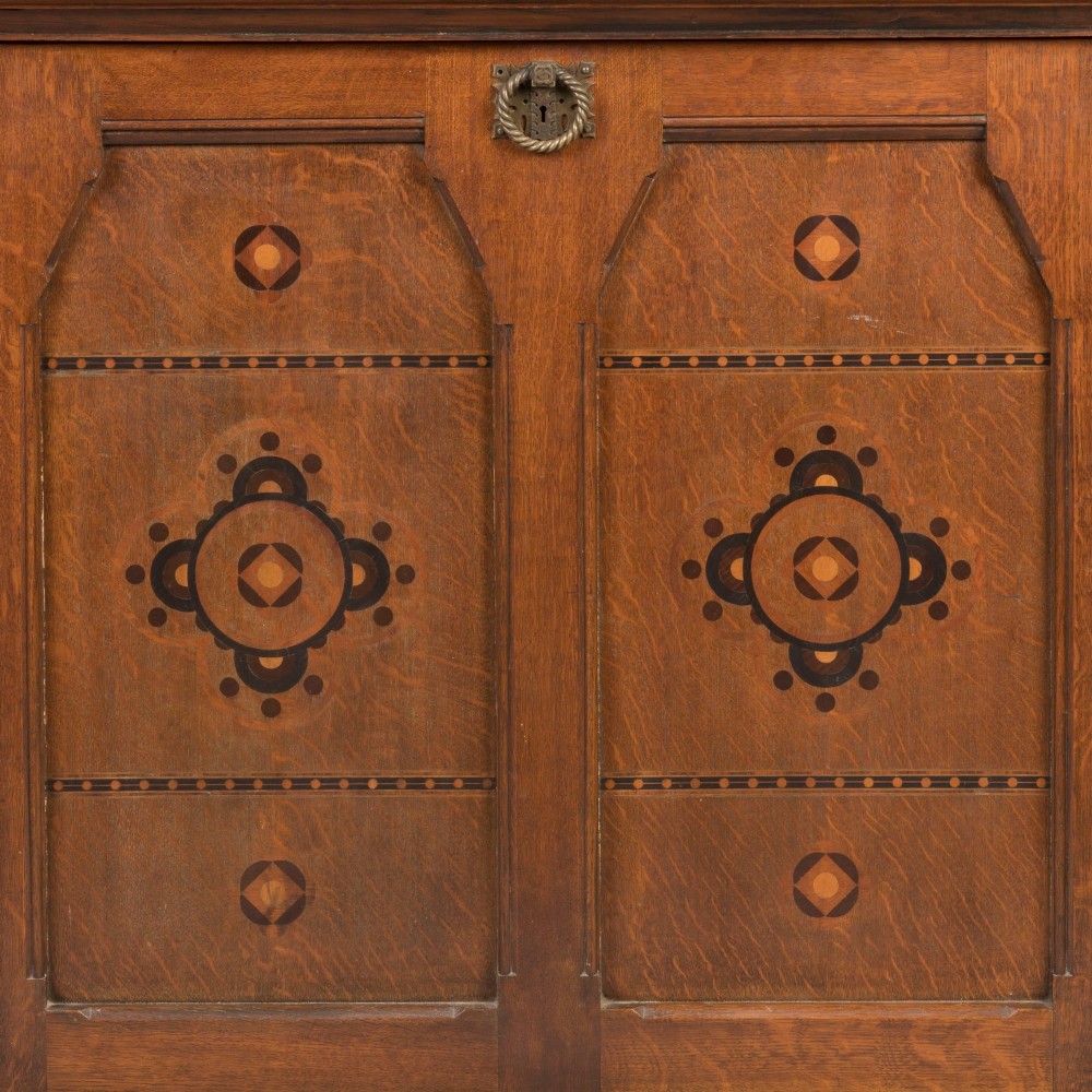 An antique Victorian Gothic Revival oak folio cabinet featuring geometric timber inlay on twin panel doors beneath an adjustable slatted display frame. View III