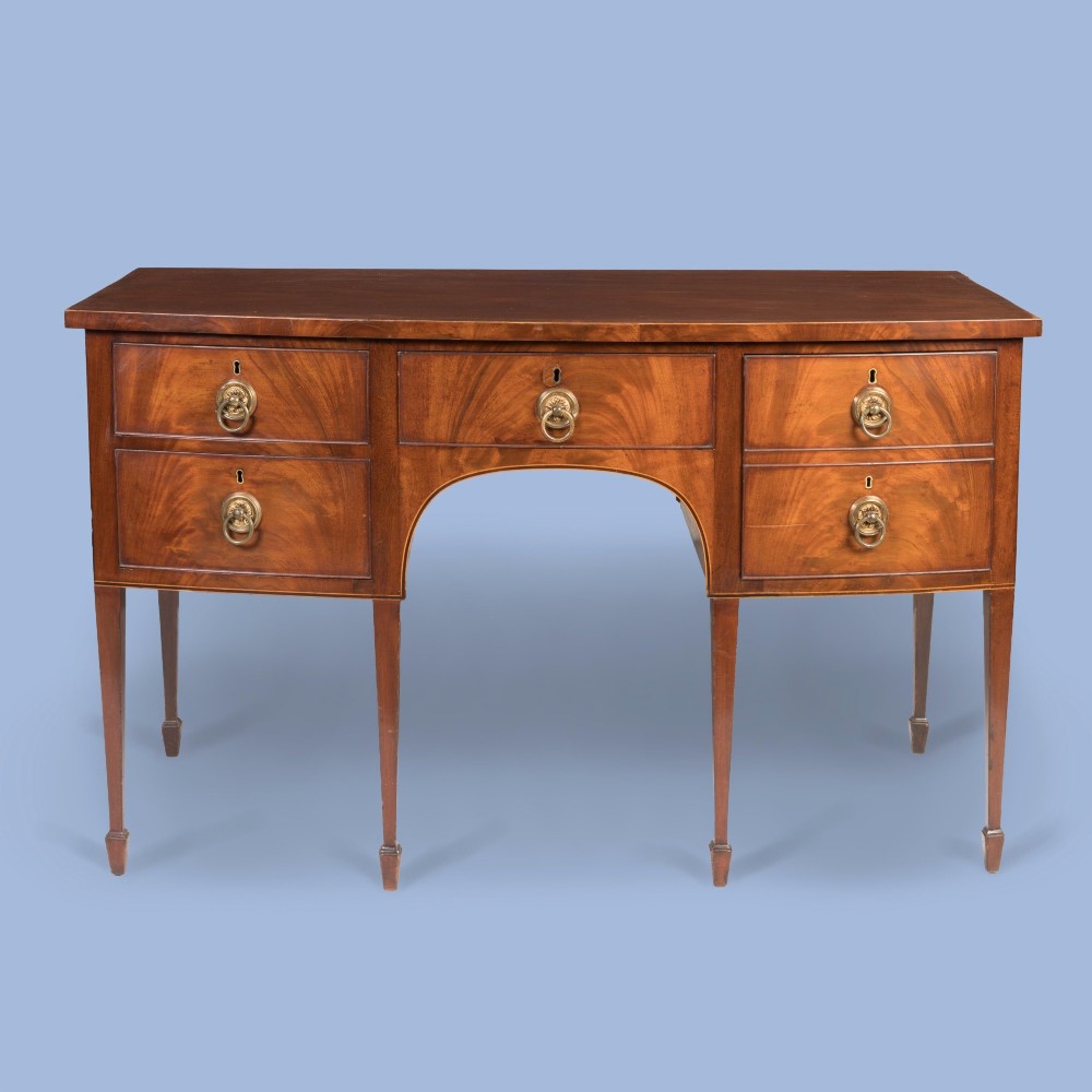 A Georgian Hepplewhite style flame mahogany sideboard featuring five drawers with brass ring handles, tapered square legs, and spade feet set against a light background.