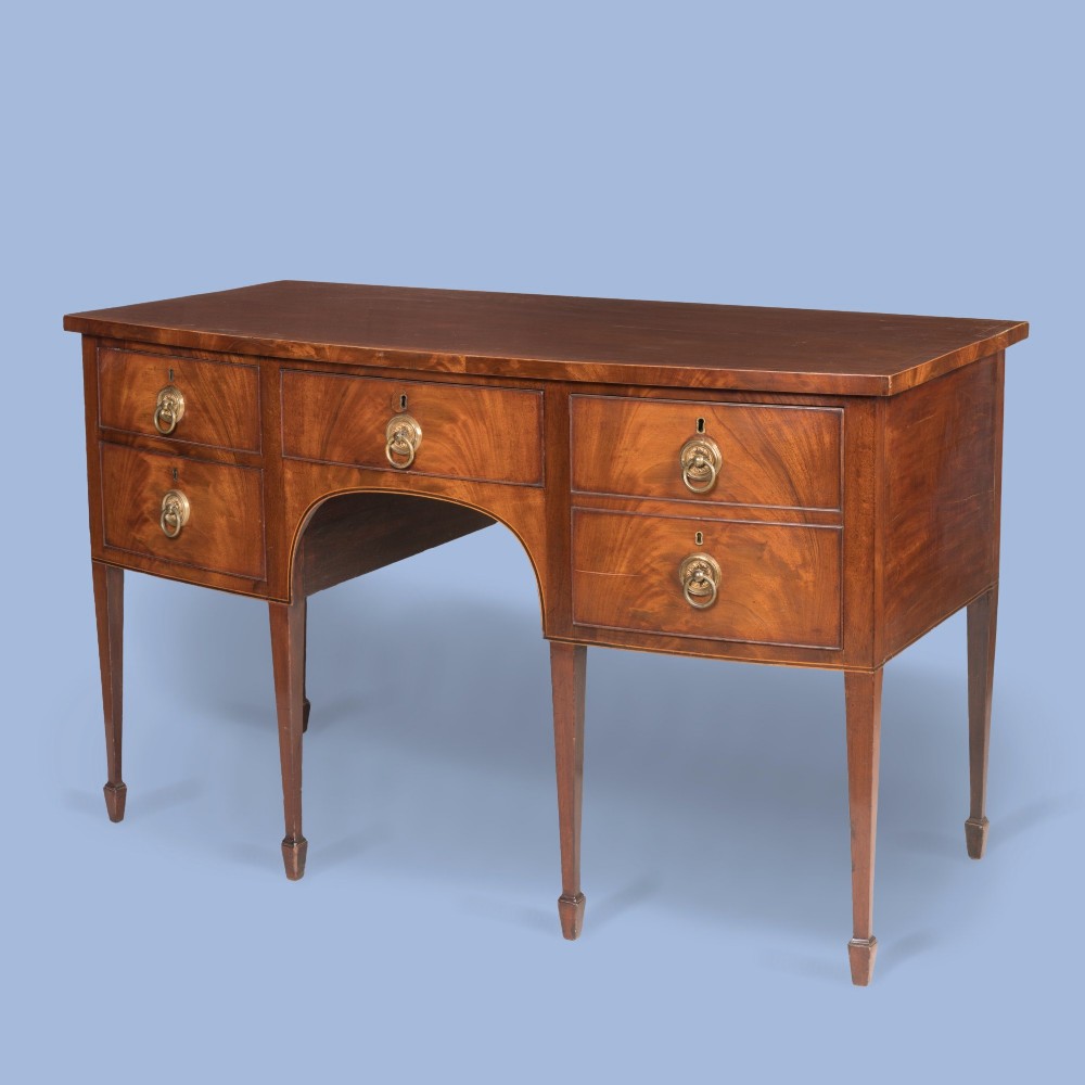 A Georgian Hepplewhite style flame mahogany sideboard featuring five drawers with brass ring handles, tapered square legs, and spade feet set against a light background. View II
