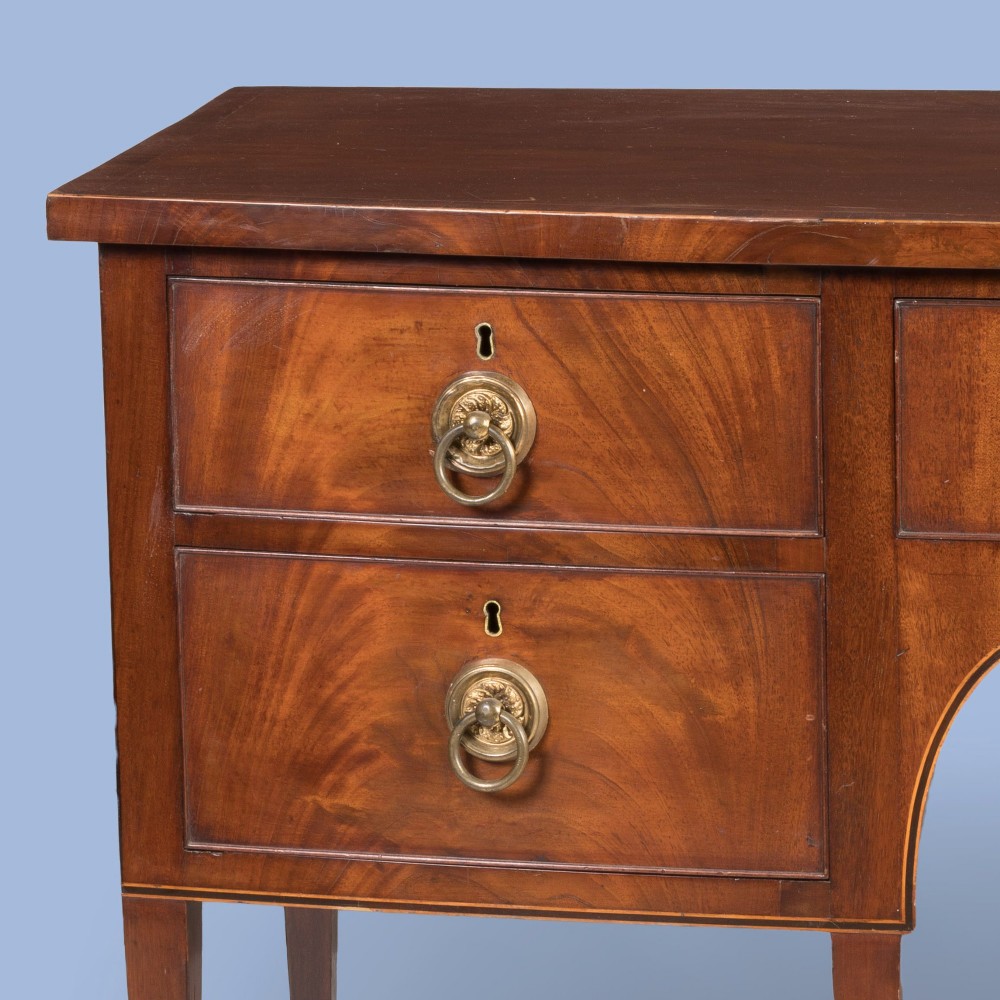 A Georgian Hepplewhite style flame mahogany sideboard featuring five drawers with brass ring handles, tapered square legs, and spade feet set against a light background. View IV