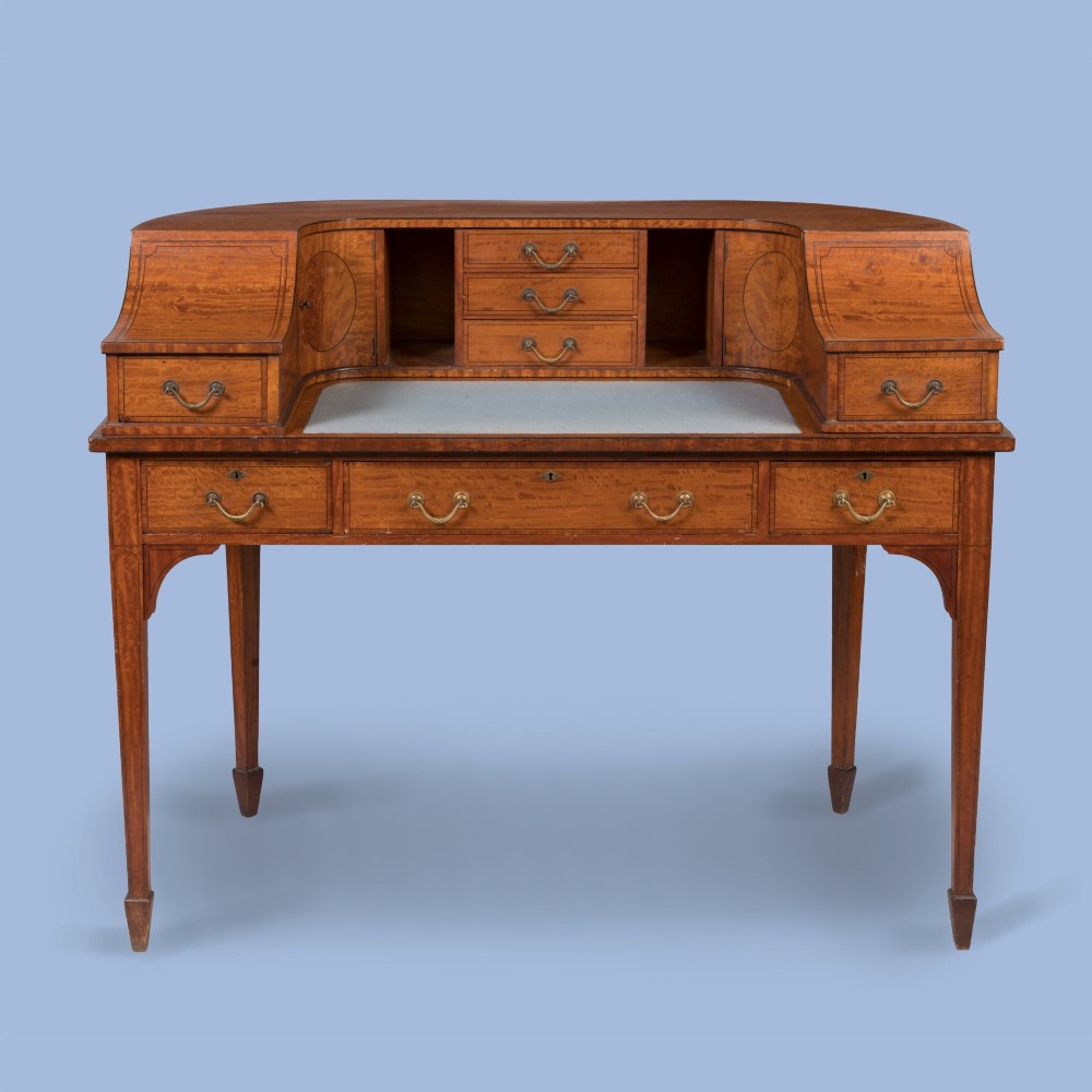 An Edwardian satinwood Carlton House desk featuring a curved rear superstructure with drawers, a leather writing surface, and square tapered legs. View II