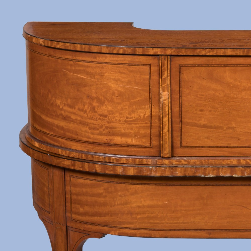 An Edwardian satinwood Carlton House desk featuring a curved rear superstructure with drawers, a leather writing surface, and square tapered legs. View IV
