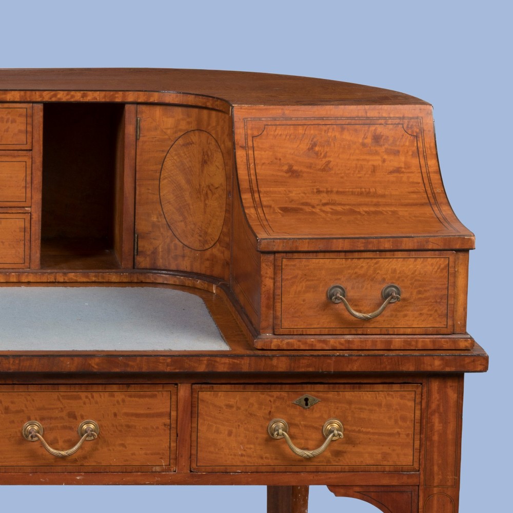 An Edwardian satinwood Carlton House desk featuring a curved rear superstructure with drawers, a leather writing surface, and square tapered legs. View V