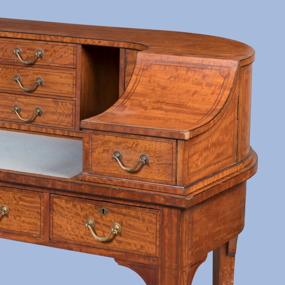 An Edwardian satinwood Carlton House desk featuring a curved rear superstructure with drawers, a leather writing surface, and square tapered legs. View VI