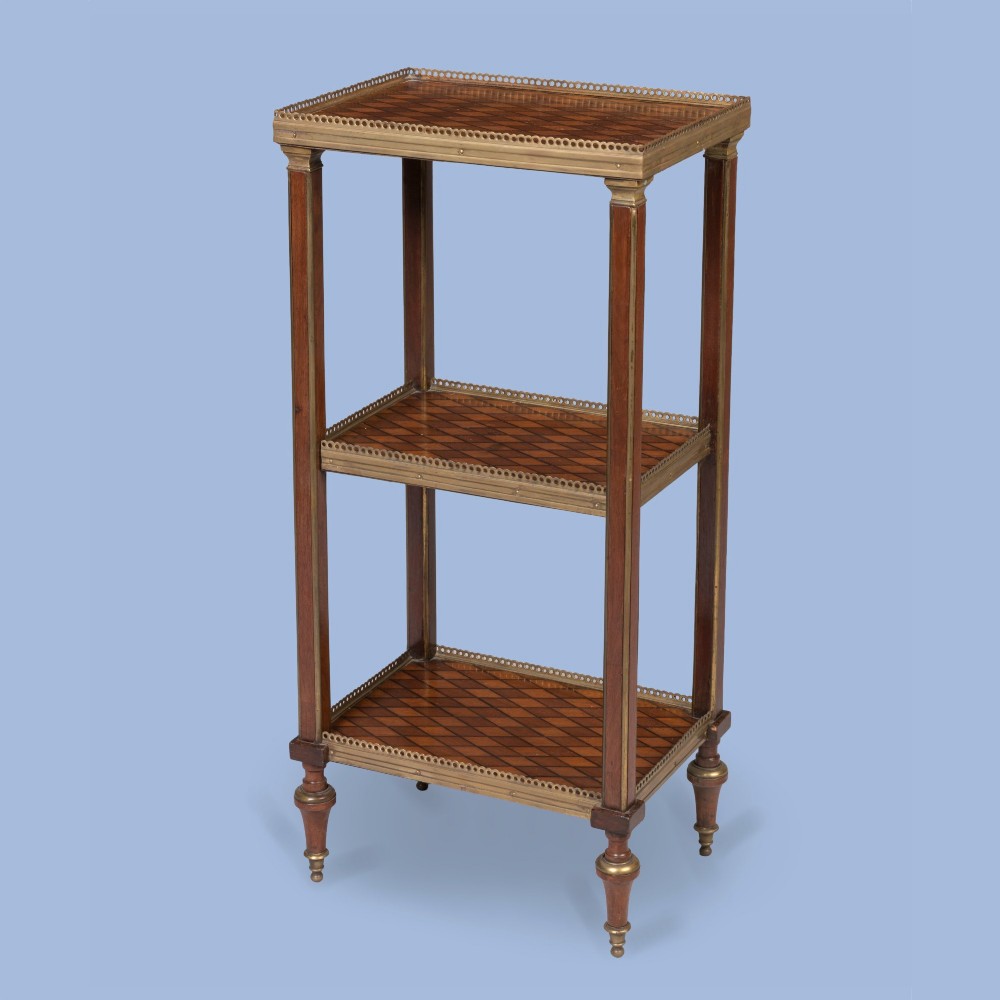 A three-tier rectangular wooden etagere featuring geometric parquetry shelves, pierced brass gallery rims, fluted corner supports, and brass-capped turned feet.