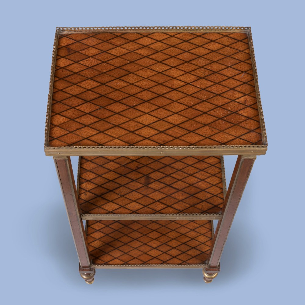 A three-tier rectangular wooden etagere featuring geometric parquetry shelves, pierced brass gallery rims, fluted corner supports, and brass-capped turned feet. View IV