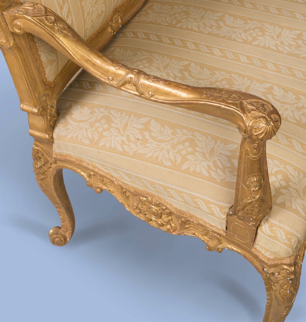 A French Louis XV style giltwood canape featuring carved floral cresting, cabriole legs, and light gold striped damask upholstery. View IV