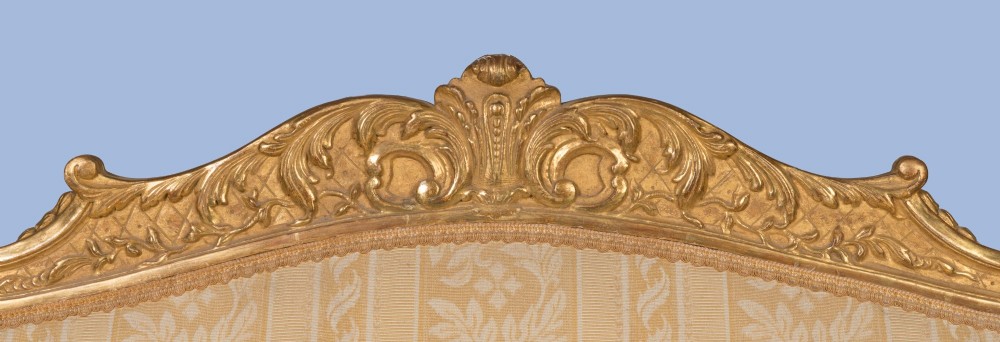 A French Louis XV style giltwood canape featuring carved floral cresting, cabriole legs, and light gold striped damask upholstery. View V