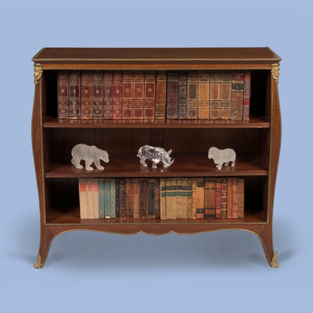 A low mahogany open bookcase featuring curved sides, adjustable shelves, a shaped apron, and gilt-bronze ormolu mounts on the corners and feet. View II
