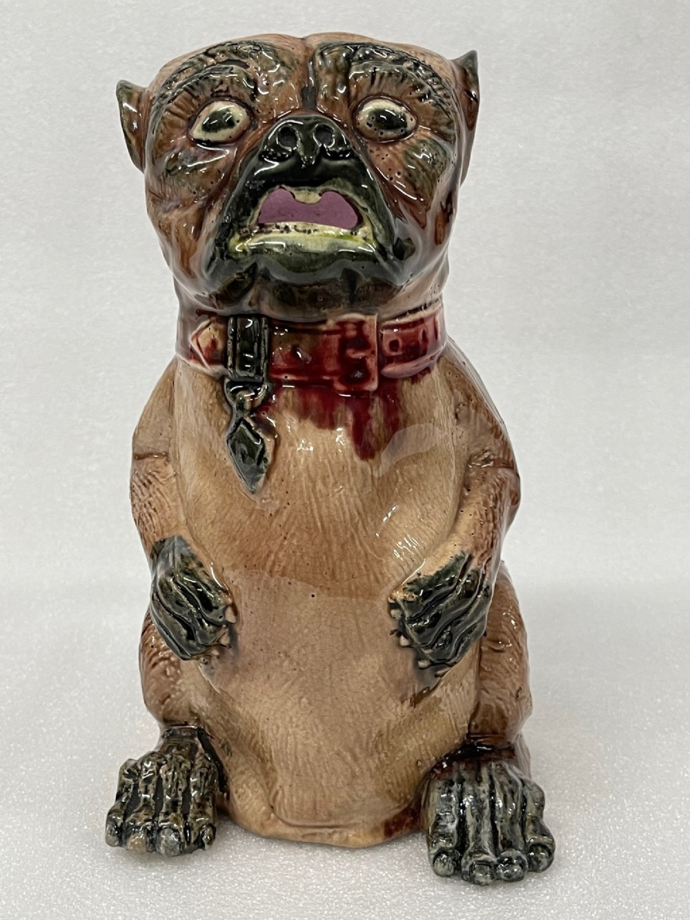 A 19th-century glazed earthenware majolica jug moulded in the form of a begging pug dog wearing a red collar.