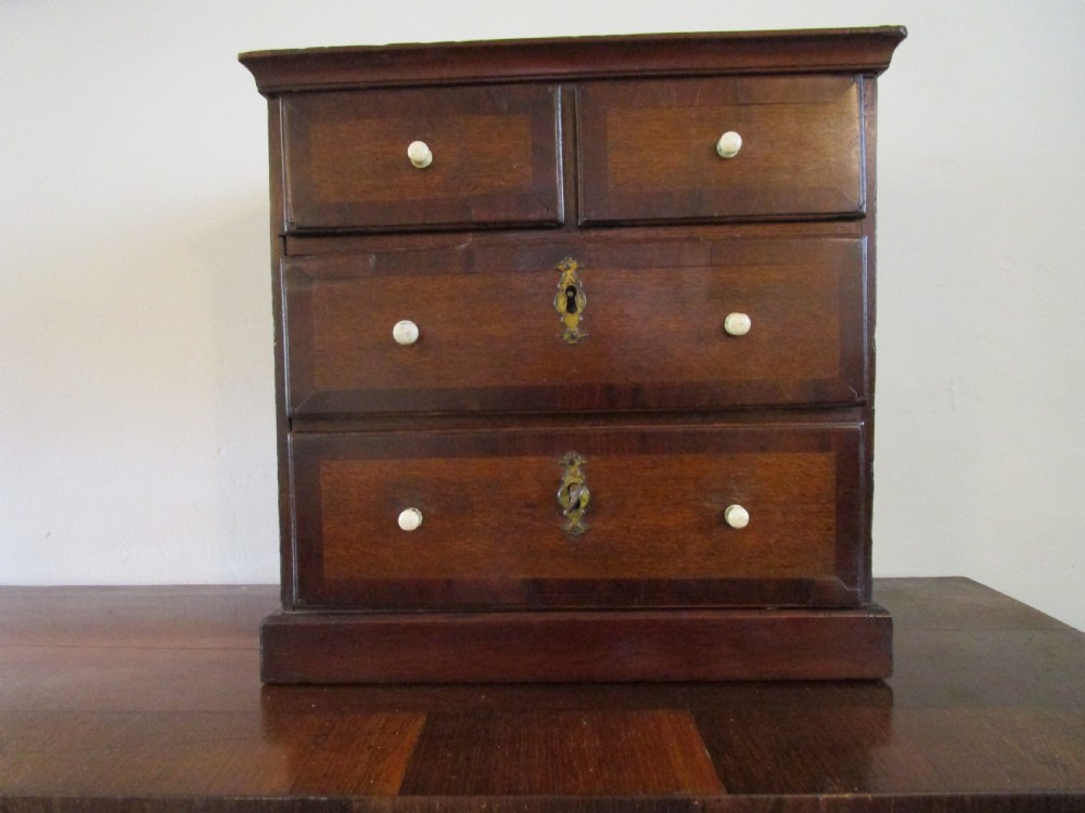 A dark mahogany miniature chest of drawers featuring two short and two long drawers with turned white knobs and brass escutcheons.
