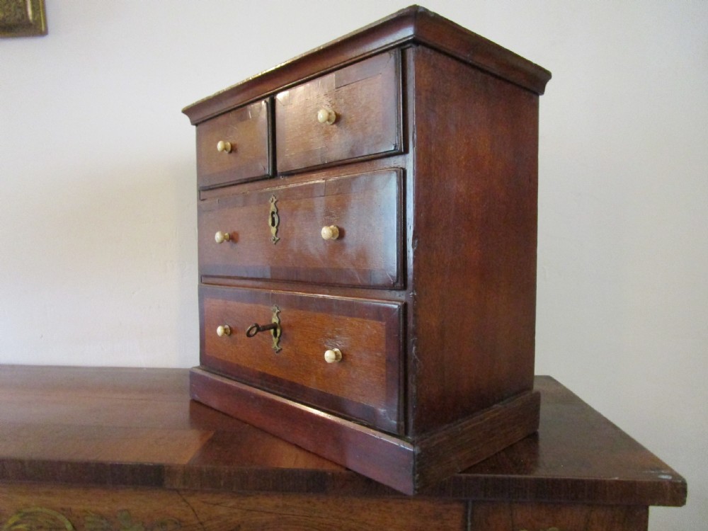 A dark mahogany miniature chest of drawers featuring two short and two long drawers with turned white knobs and brass escutcheons. View II