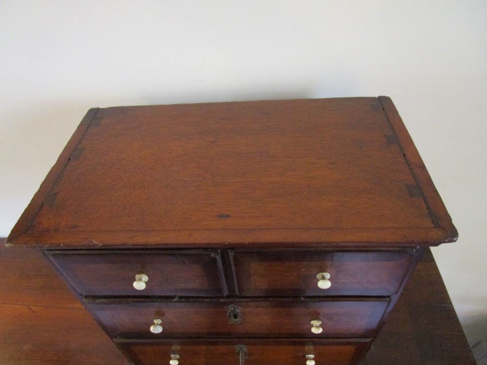 A dark mahogany miniature chest of drawers featuring two short and two long drawers with turned white knobs and brass escutcheons. View IV