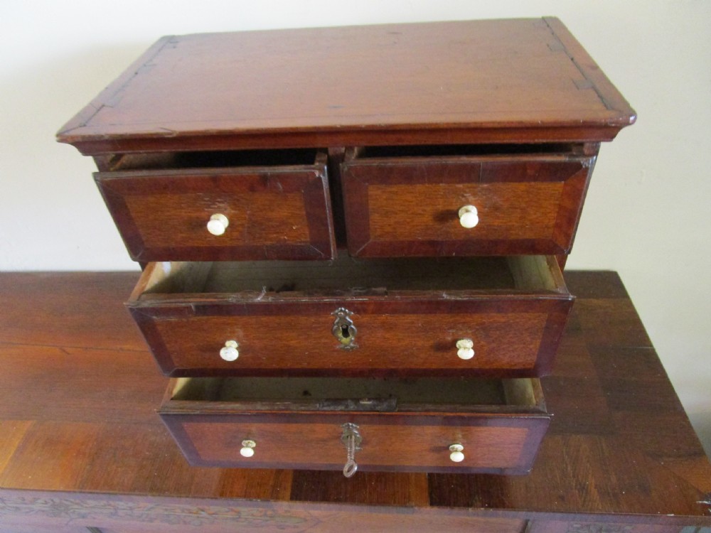 A dark mahogany miniature chest of drawers featuring two short and two long drawers with turned white knobs and brass escutcheons. View V