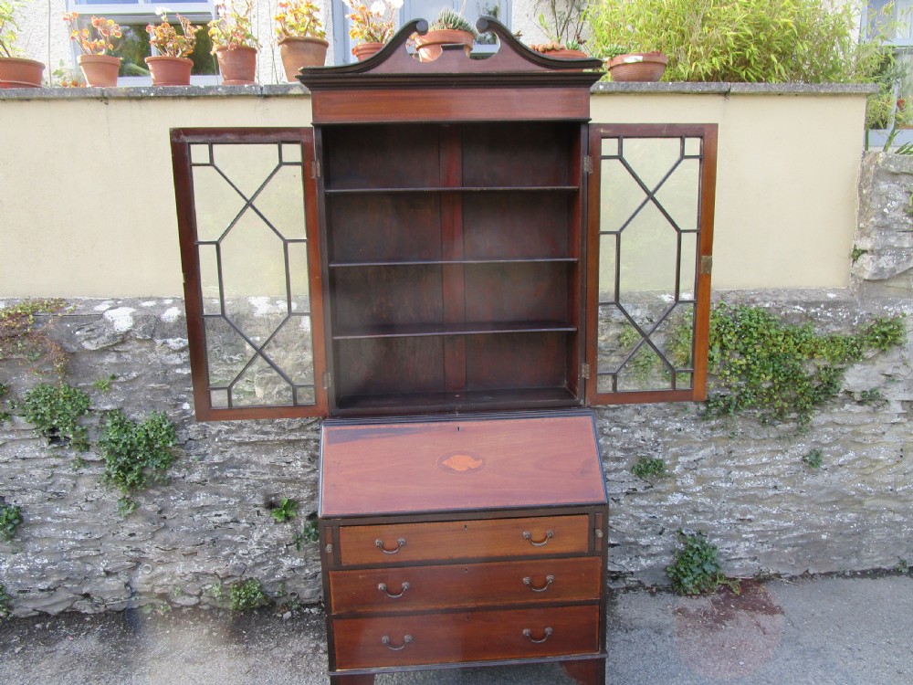 An antique mahogany bureau bookcase with a swan-neck pediment, geometric glazed cabinet doors, an inlaid fall-front writing slope, and three lower drawers. View VI