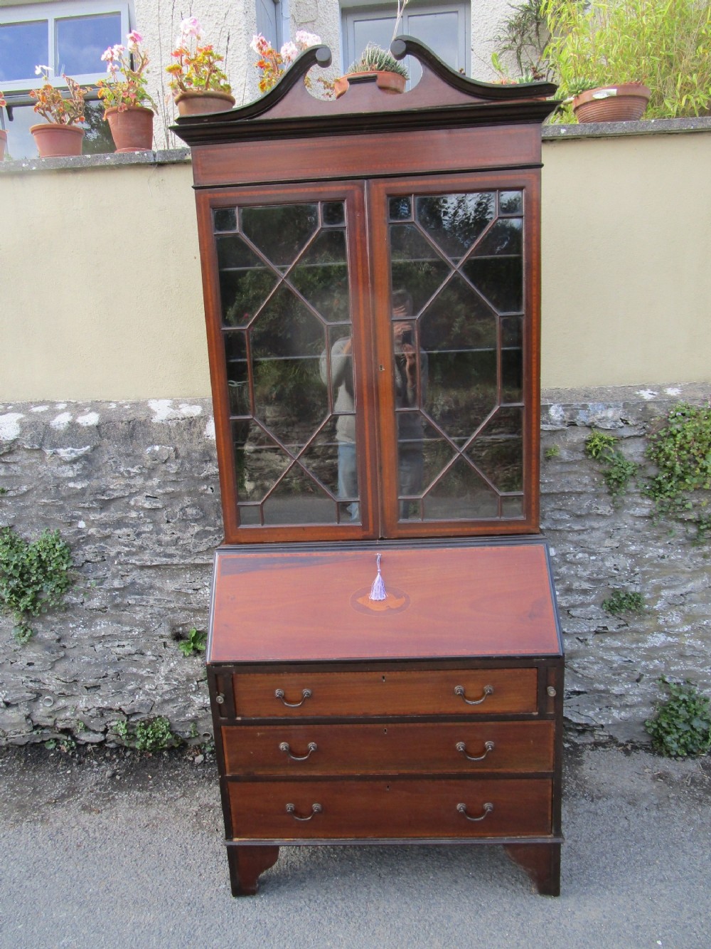 An antique mahogany bureau bookcase with a swan-neck pediment, geometric glazed cabinet doors, an inlaid fall-front writing slope, and three lower drawers.