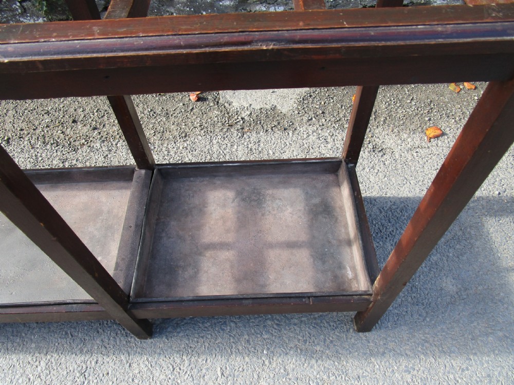 A long, dark wood stick stand featuring a grid of rectangular compartments at the top and sectioned metal drip trays at the base. View IV